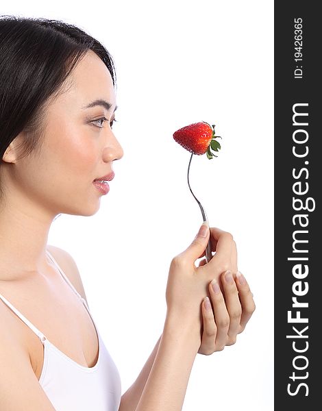 Beautiful smiling chinese teenager girl in profile, holding up a fresh red strawberry fruit on a fork. Beautiful smiling chinese teenager girl in profile, holding up a fresh red strawberry fruit on a fork.