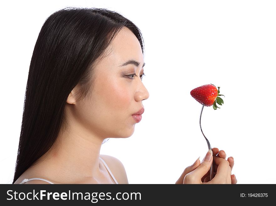 Beautiful young oriental teenager girl in profile, holding up a fresh red strawberry fruit on a fork. Beautiful young oriental teenager girl in profile, holding up a fresh red strawberry fruit on a fork.