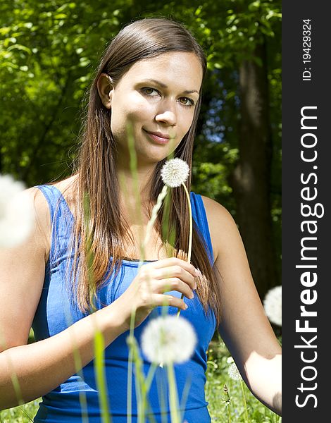 Beautiful young girl in the park smelling dandelion