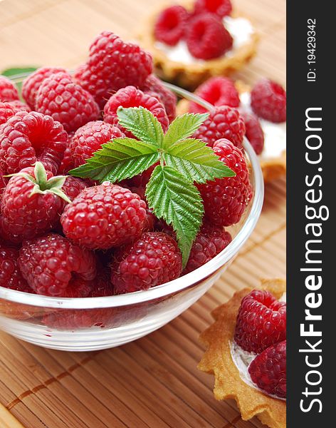 Fresh raspberries in glass bowl with leaf and raspberry muffins on the straw mat. Fresh raspberries in glass bowl with leaf and raspberry muffins on the straw mat