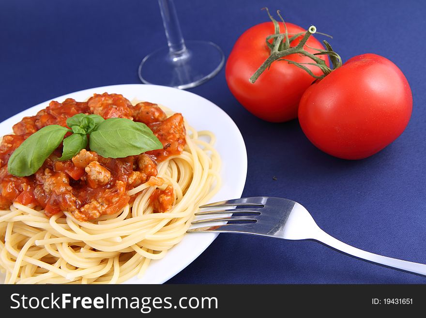Spaghetti bolognese on a plate, a fork, wineglass and tomatoes