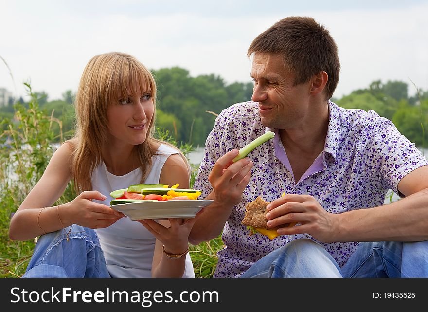 Young happy couple eating together outdoors. Young loving couple having a picnic outdoors