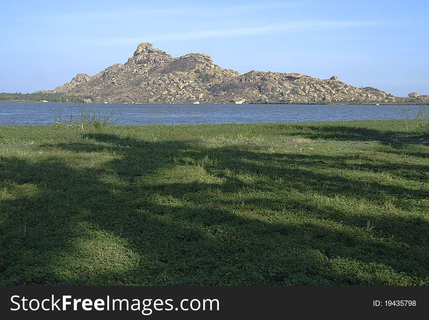 Distant rocky hill and lake with shaded lush green grassy land in foreground. Distant rocky hill and lake with shaded lush green grassy land in foreground