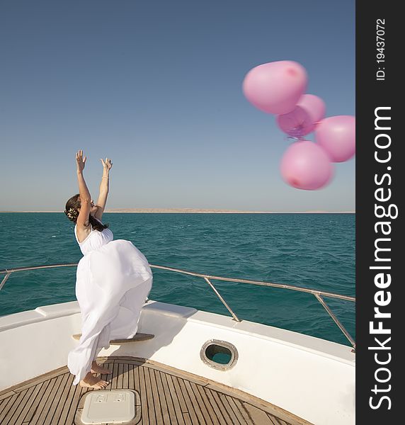 Newly married bride releasing a bunch of balloons while standing on the front of a boat. Newly married bride releasing a bunch of balloons while standing on the front of a boat