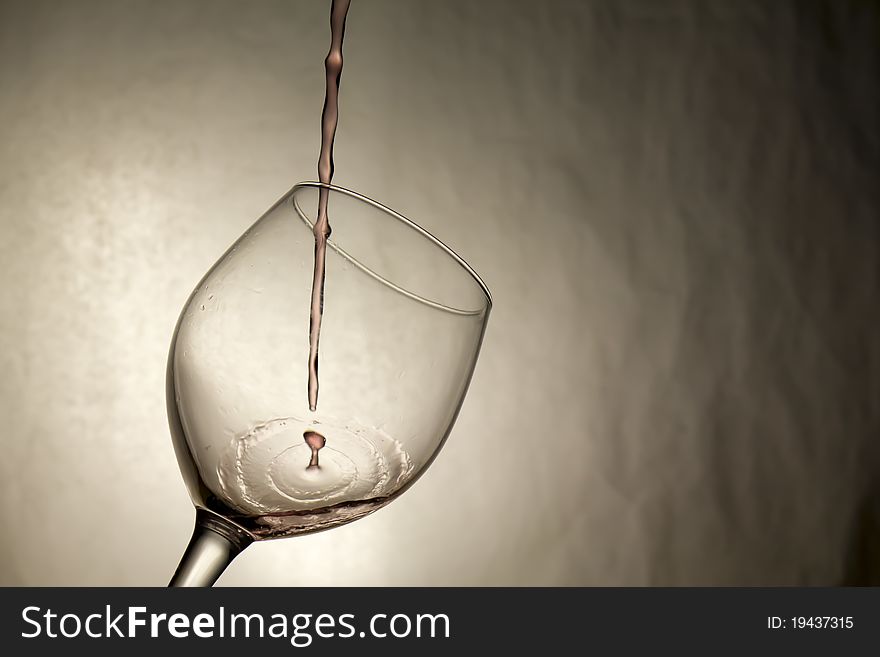 The first drop of wine being poured splashes into a wine glass. The first drop of wine being poured splashes into a wine glass
