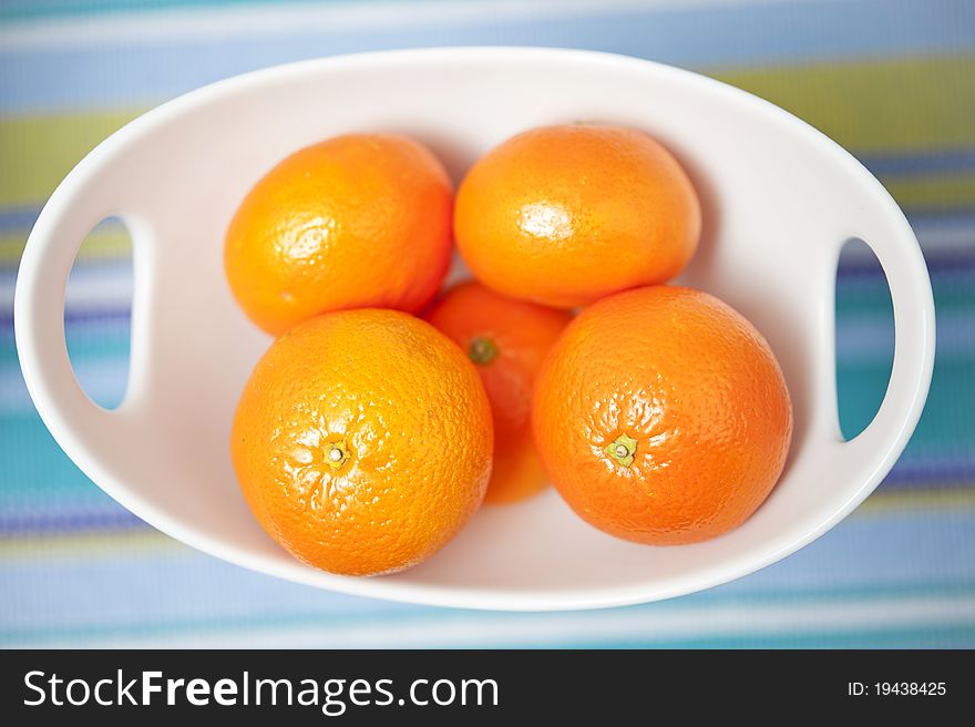 Fresh oranges in a white bowl over multicolor background.