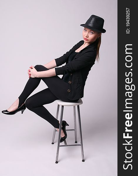 Beautiful young woman in black suit sits on chair.