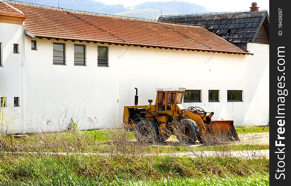 Yellow bulldozer by white building with red tiled roof