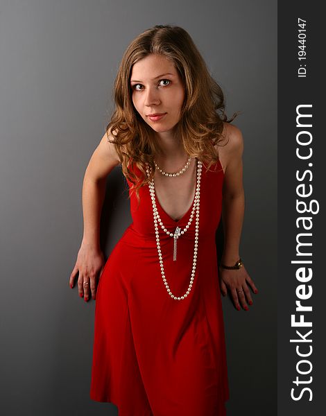 Girl in red dress posing at grey wall bending forward. Girl in red dress posing at grey wall bending forward.