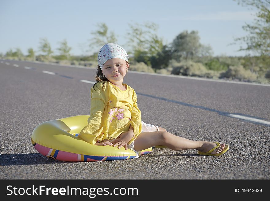 Little Girl Sitting On Asphalted Road