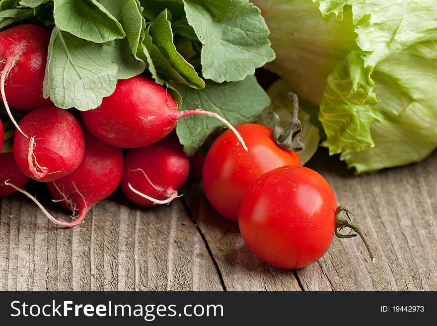 Bunch of fresh radishes, gren salad and tomato on old wooden table. Bunch of fresh radishes, gren salad and tomato on old wooden table