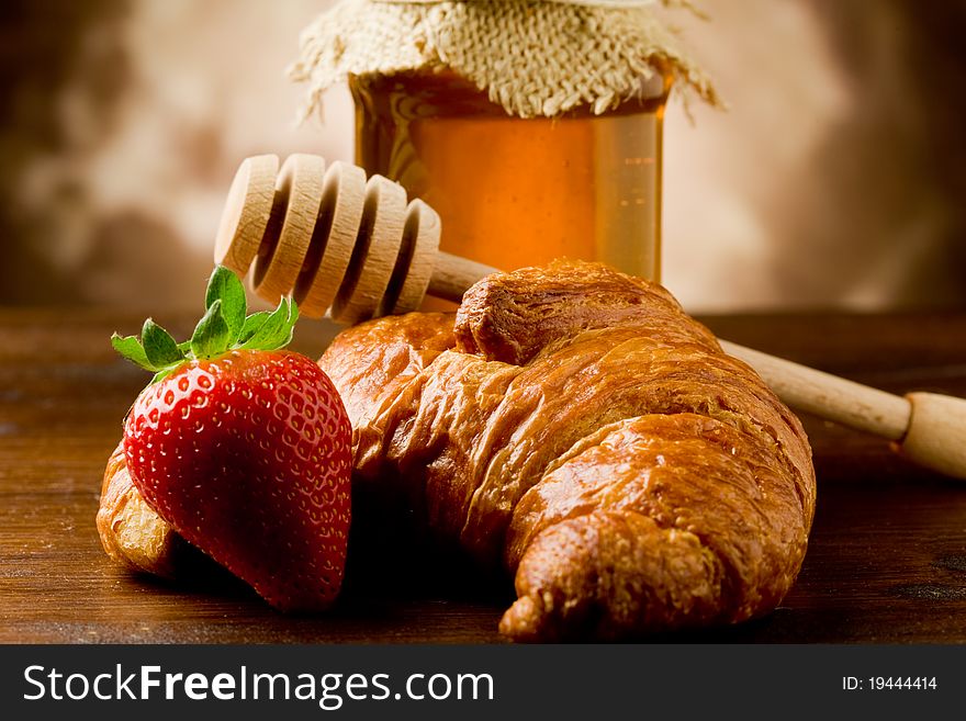 Photo of croissants with honey and strawberries on wooden table