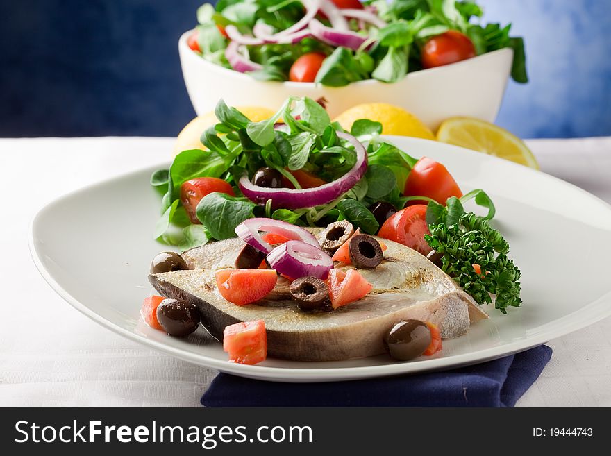 Grilled swordfish with mixed salad on white towel in front of blue background