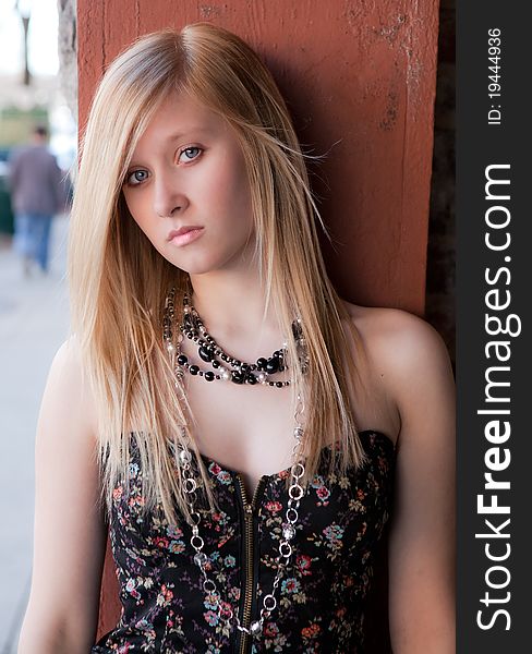 A portrait of a lovely young woman in a tube top and necklaces, posing against a wall in the downtown of a city. A portrait of a lovely young woman in a tube top and necklaces, posing against a wall in the downtown of a city