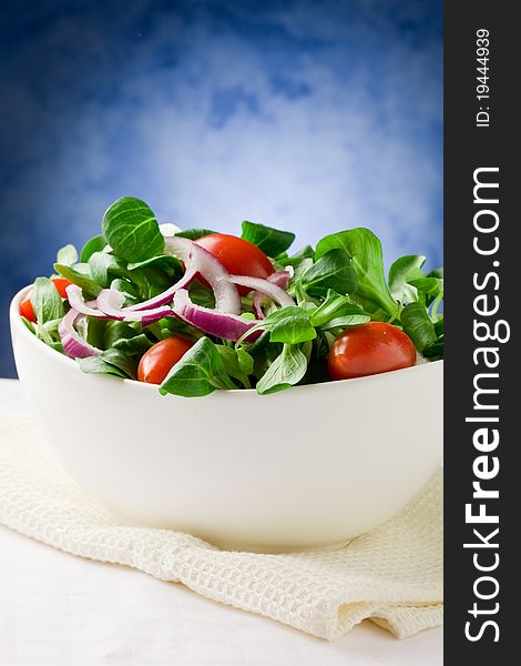 Colorful mixed salad inside a bowlo on white towel in front of blue background