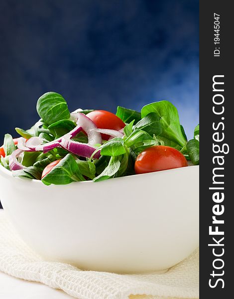 Colorful mixed salad inside a bowlo on white towel in front of blue background