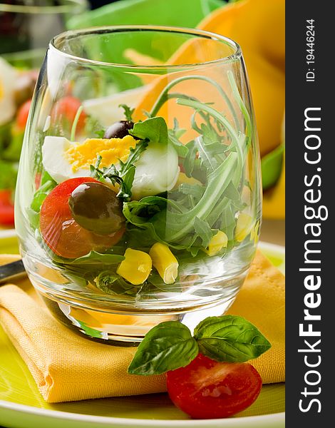 Delicious starter of mixed salad inside a glass on green wooden table