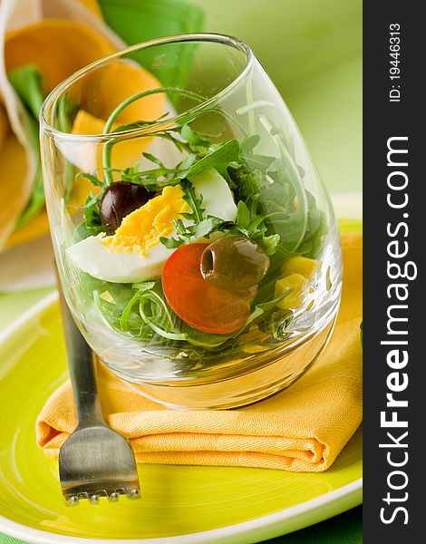 Delicious starter of mixed salad inside a glass on green wooden table