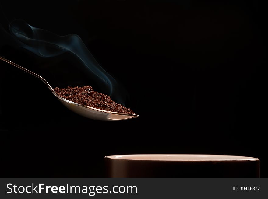 Teaspoon freshly roasted and ground coffee over the mug. Photographed on a black background. Teaspoon freshly roasted and ground coffee over the mug. Photographed on a black background.