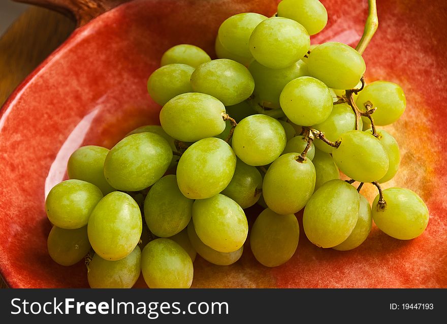 Bunch of green grapes in a light red dish. Bunch of green grapes in a light red dish