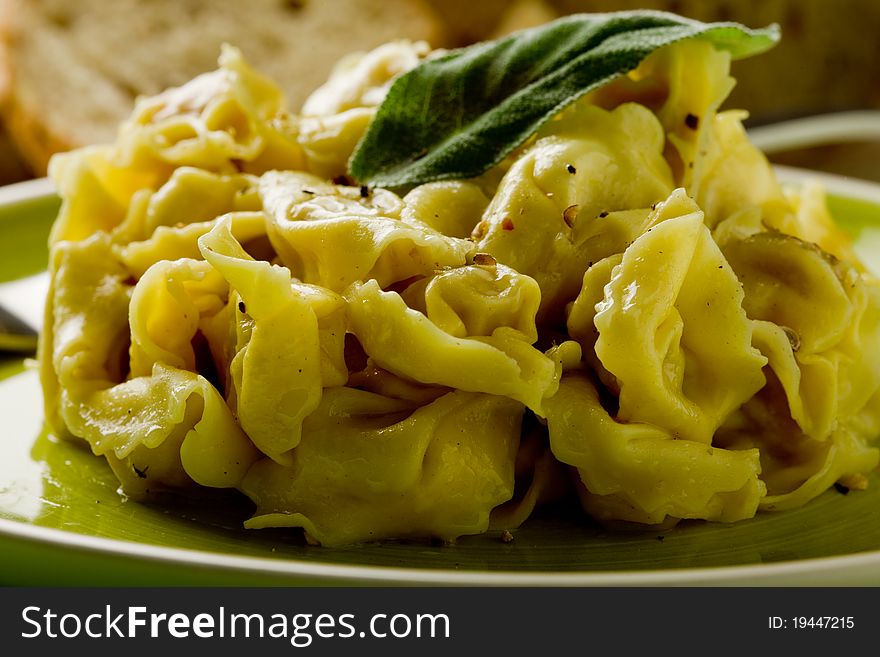 Delicious italian fresh tortellini with butter and sage on green wooden table