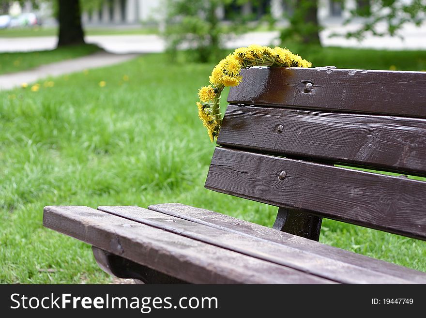 Wreath of yellow dandelions hanging on the back of a wooden park bench. Wreath of yellow dandelions hanging on the back of a wooden park bench