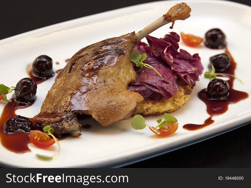 Roasted duck leg with cherries on a black background. Roasted duck leg with cherries on a black background.