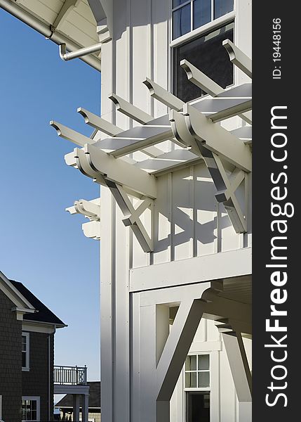 A window arbor is seen attached to a covered porch of a home. There is an open window above it. Vertical shot.