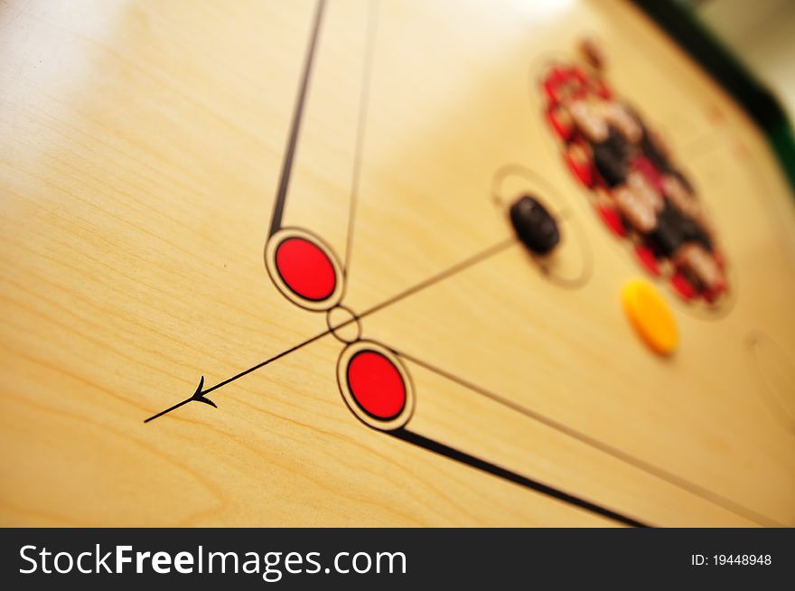 Photo of Carrom board with striker and coins. Focus at the arrow