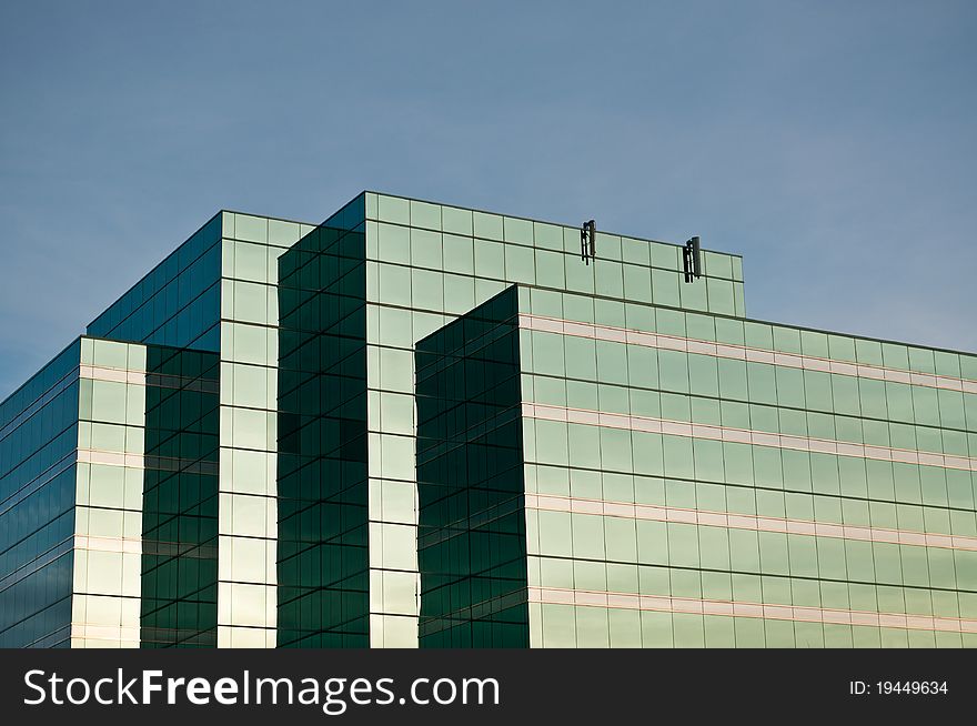 A mirrored glass office building stands in front of a blue sky. A mirrored glass office building stands in front of a blue sky.