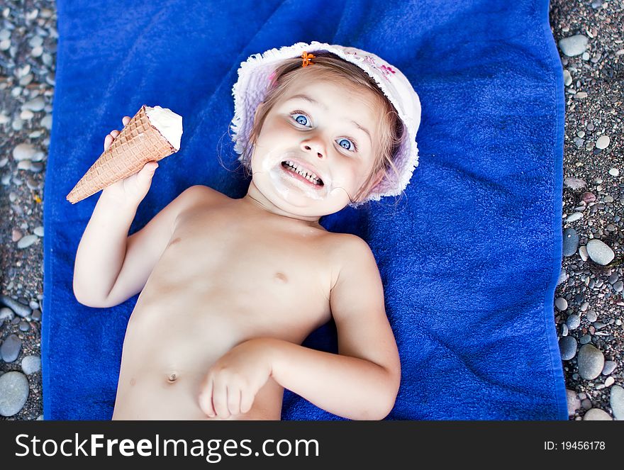 Little girl with an ice-cream laying on a towel