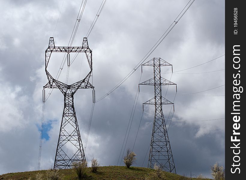 Electricity transmission towers stand on a hillside in the path of an oncoming storm. Electricity transmission towers stand on a hillside in the path of an oncoming storm.
