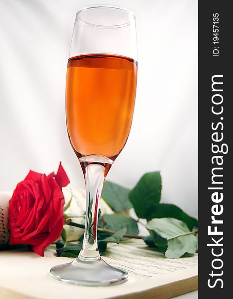 Red rose and champagne on a musical score background creating a romantic mood. Red rose and champagne on a musical score background creating a romantic mood.