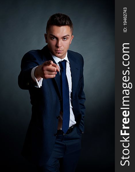 Fashion businessman pointing at the camera on a dark background