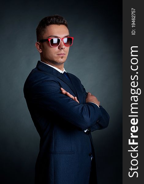 Confident fashion business man in red sunglasses standing with hands crossed