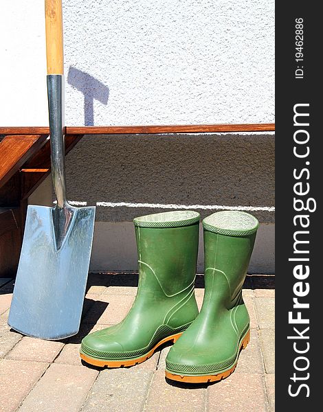 Rubber boots and spade in front of a brown bench