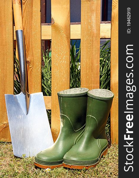 Rubber boots and spade in front of a brown fence