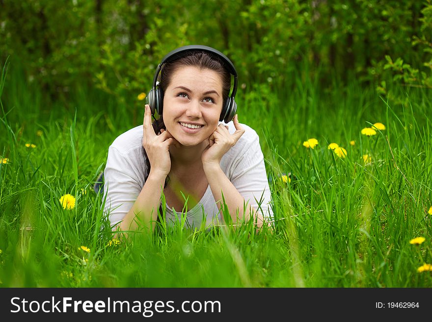 Pretty smiling woman listening musik on the grass and looking up, with space for text, background out of focus. Pretty smiling woman listening musik on the grass and looking up, with space for text, background out of focus