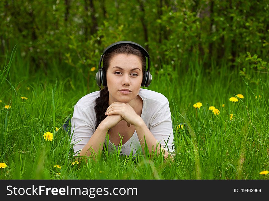 Pretty woman listening musik on the grass and looking streight, with space for text, background out of focus. Pretty woman listening musik on the grass and looking streight, with space for text, background out of focus