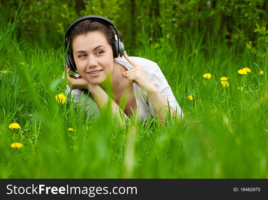 Pretty smiling woman listening musik on the grass and looking right, with space for text, background out of focus. Pretty smiling woman listening musik on the grass and looking right, with space for text, background out of focus