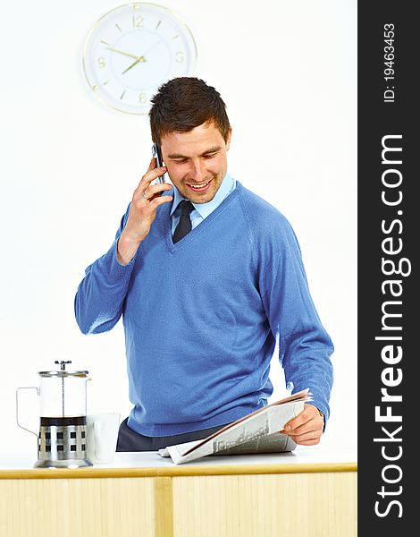 Businessman in kitchen talking by mobile phone, reading newspaper and smiling. Businessman in kitchen talking by mobile phone, reading newspaper and smiling