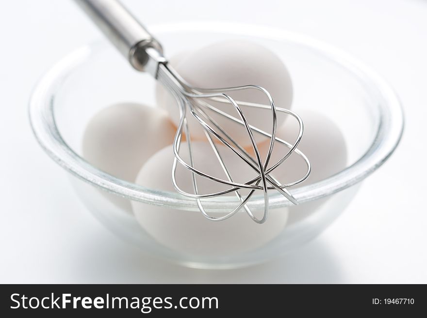 Metal whisk and fresh eggs in bowl, over white background.