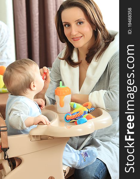 A mother is feeding her baby in the highchair at home. A mother is feeding her baby in the highchair at home.