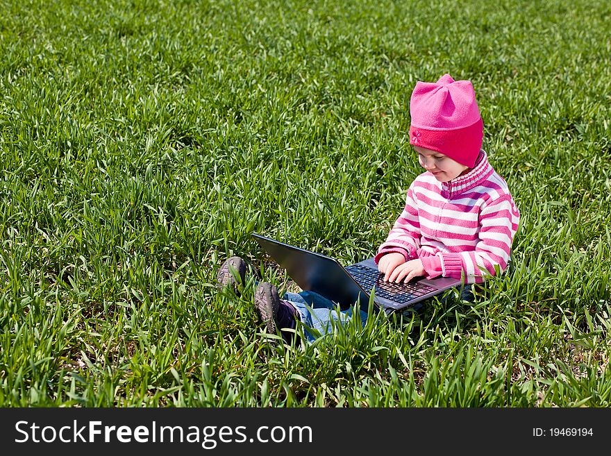 Little girl sitting with a laptop on a grass. Little girl sitting with a laptop on a grass