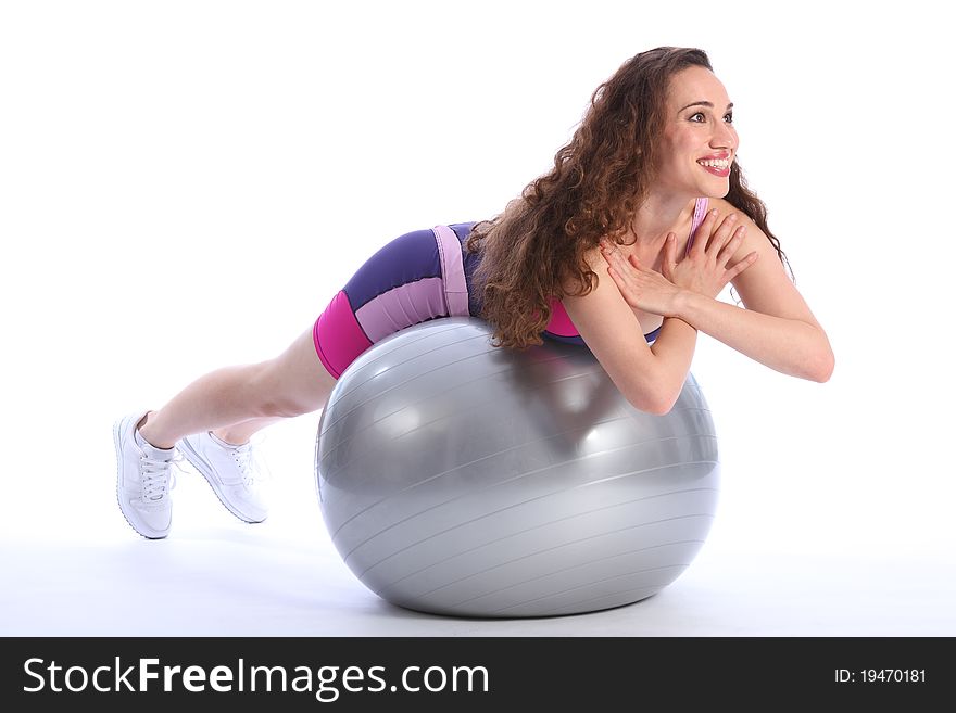 Beautiful brunette woman with big smile lying on top of fitness exercise ball for balance during workout. She is wearing bright blue and pink sports clothes and white trainers. Beautiful brunette woman with big smile lying on top of fitness exercise ball for balance during workout. She is wearing bright blue and pink sports clothes and white trainers.