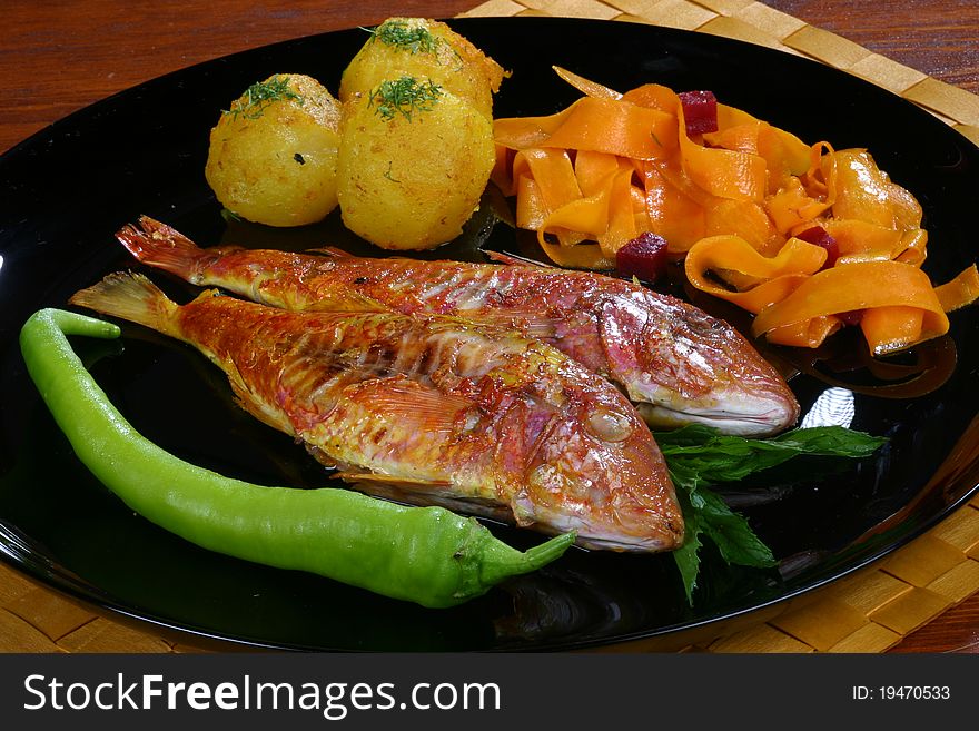 Fish with potatoes and pepper on a black plate