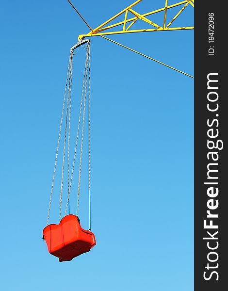 The armchair of a children's roundabout hanging on chains, against the blue bright sky