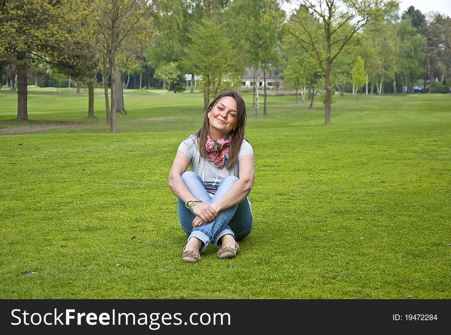 Beautiful attractive woman sitting on a green grass golf course. Smiles.