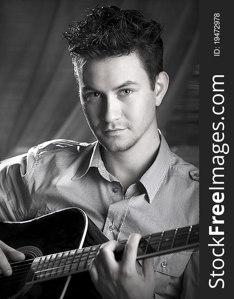 Classy romantic guy sitting on a chair with a guitar in his hands. Black and white photography. Classy romantic guy sitting on a chair with a guitar in his hands. Black and white photography.