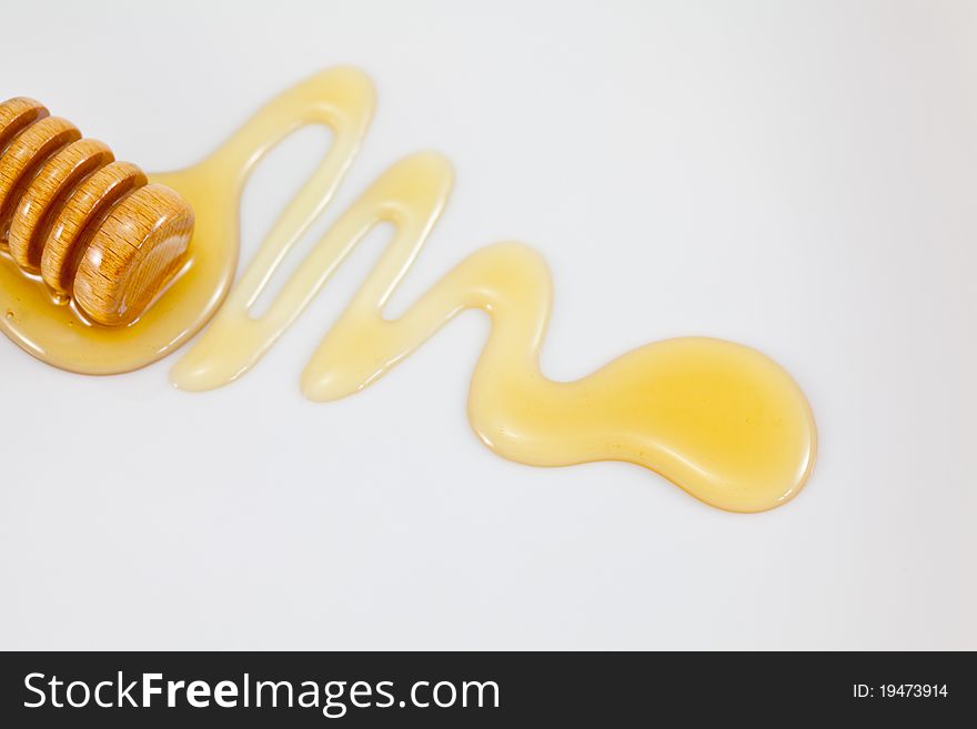 A honey dipper and a trail of honey on a neutral background. A honey dipper and a trail of honey on a neutral background.